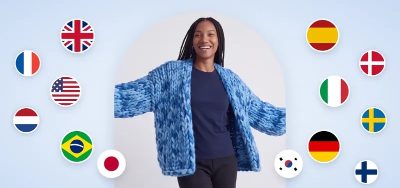 Una donna sorridente con il cardigan a maglia grossa Blue Fairy, braccia aperte, circondata da tredici bandiere.