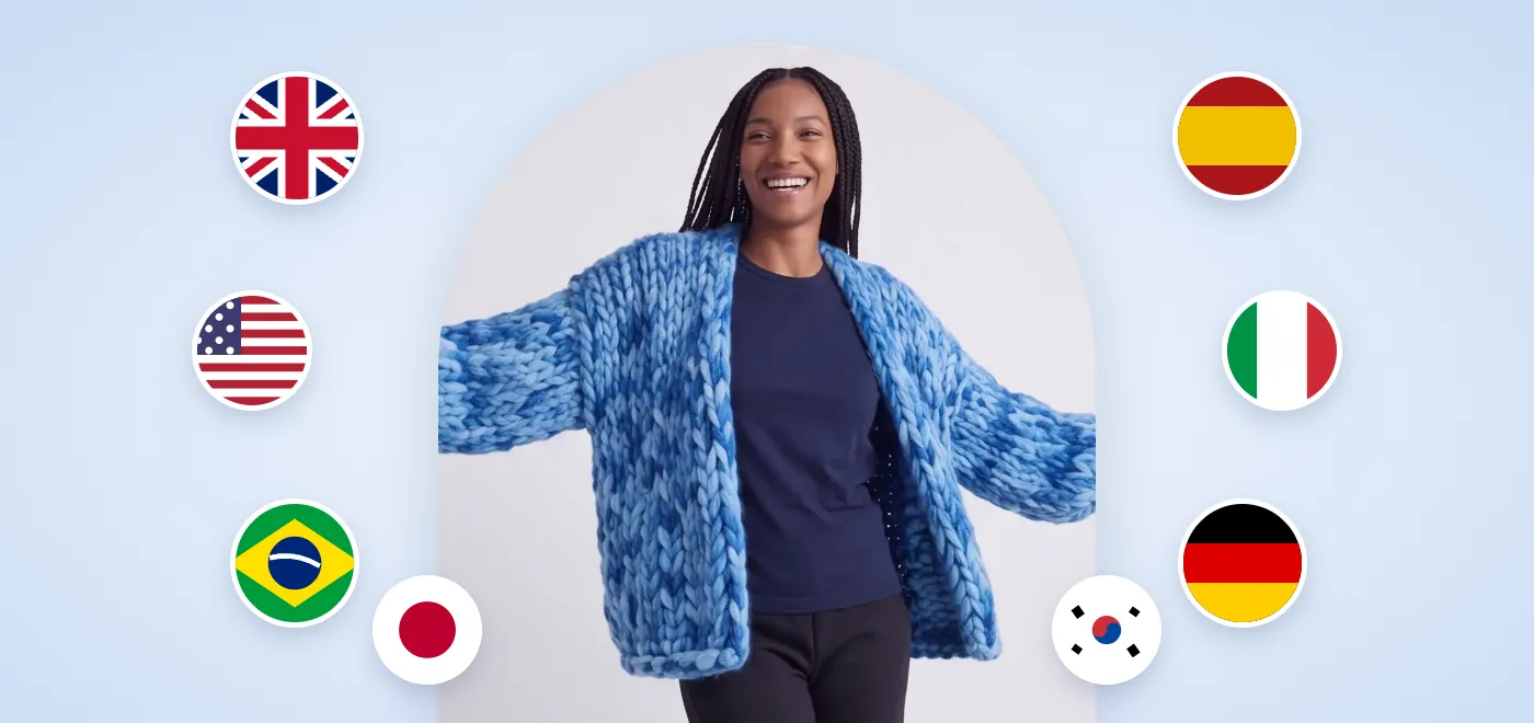 A smiling woman spreads her arms wide in the Blue Fairy chunky knit cardigan, surrounded by the flags of the UK, the US, Brazil, Spain, Italy, Germany, Japan and South Korea.