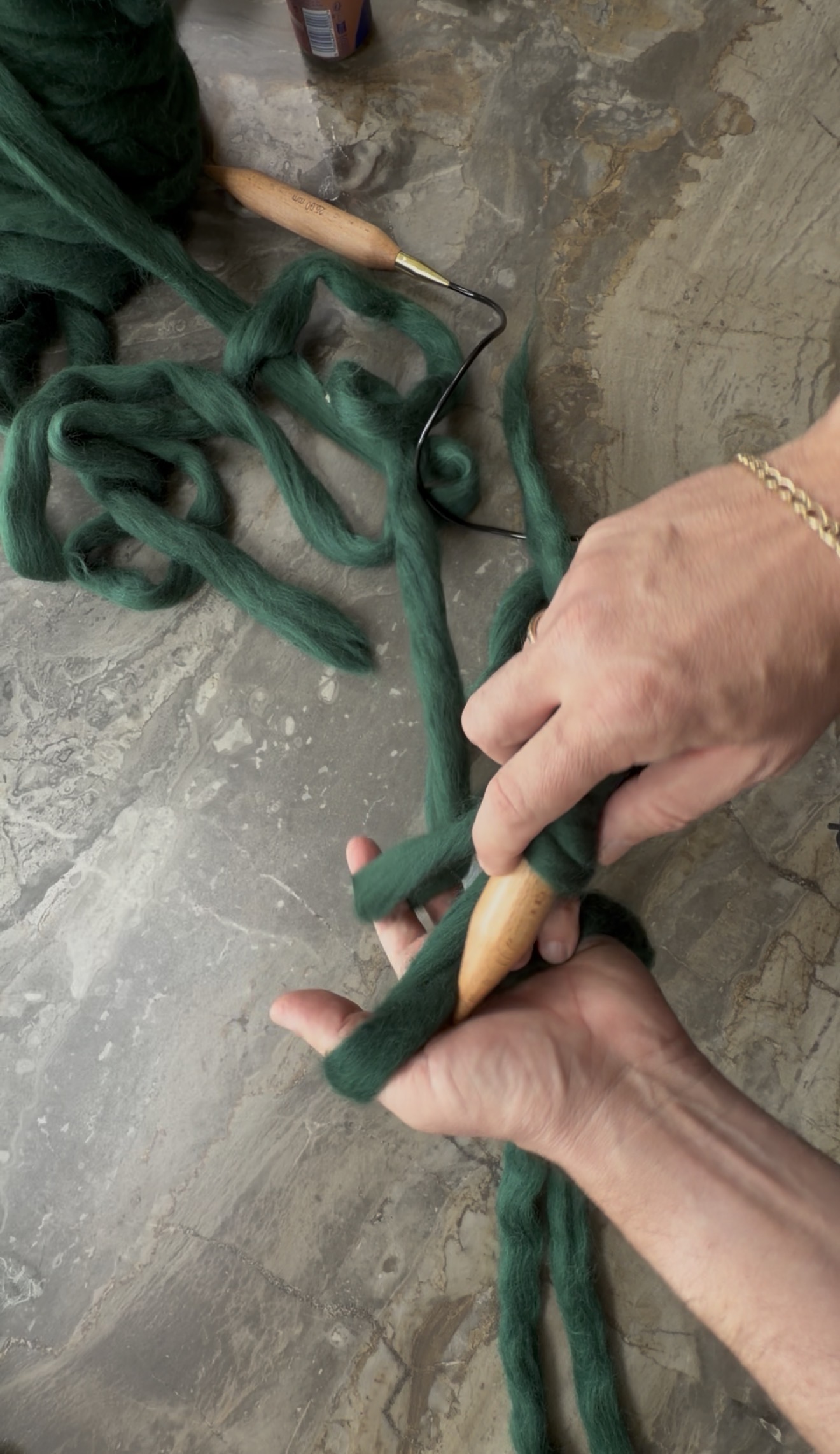 Hands casting on giant green roving onto a 25mm wooden needle, keeping the loops loose