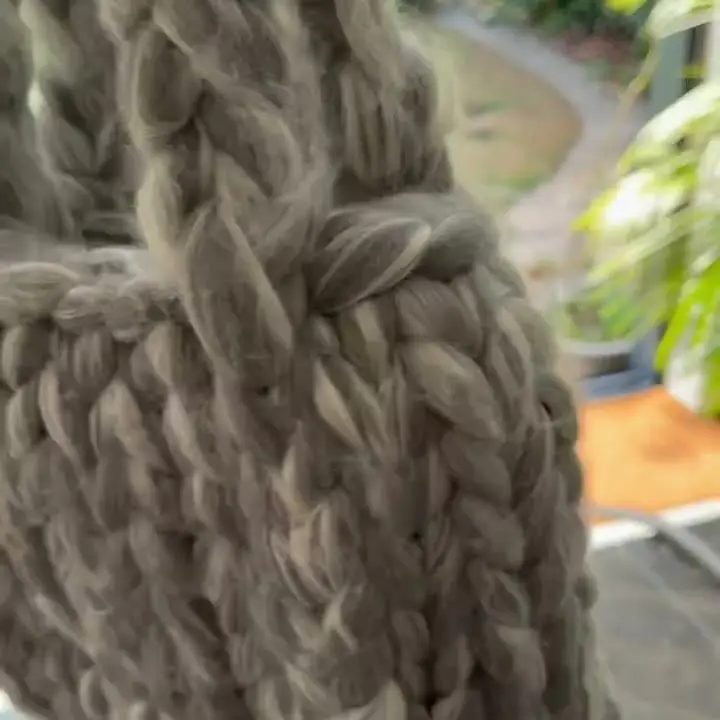 The silver-grey merino-silk mini bag held up by its handles in front of a garden window.