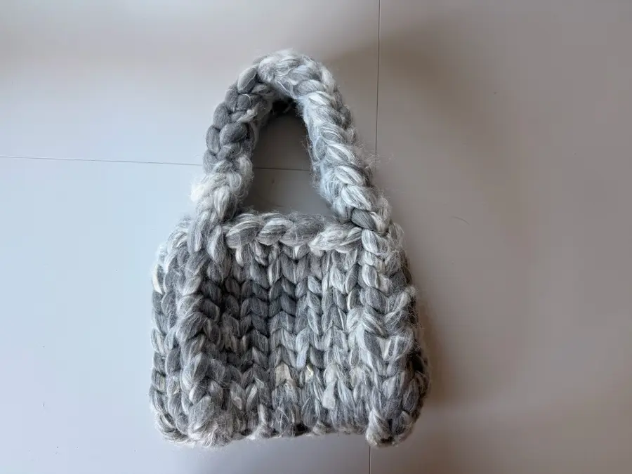 The finished silver-grey merino-silk chunky mini bag, photographed from above on a white table.