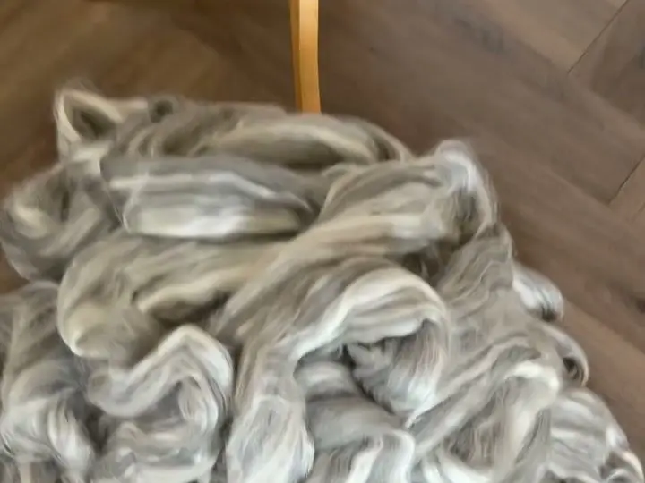 A pile of silver-grey merino-silk roving laid out on a herringbone wooden floor.
