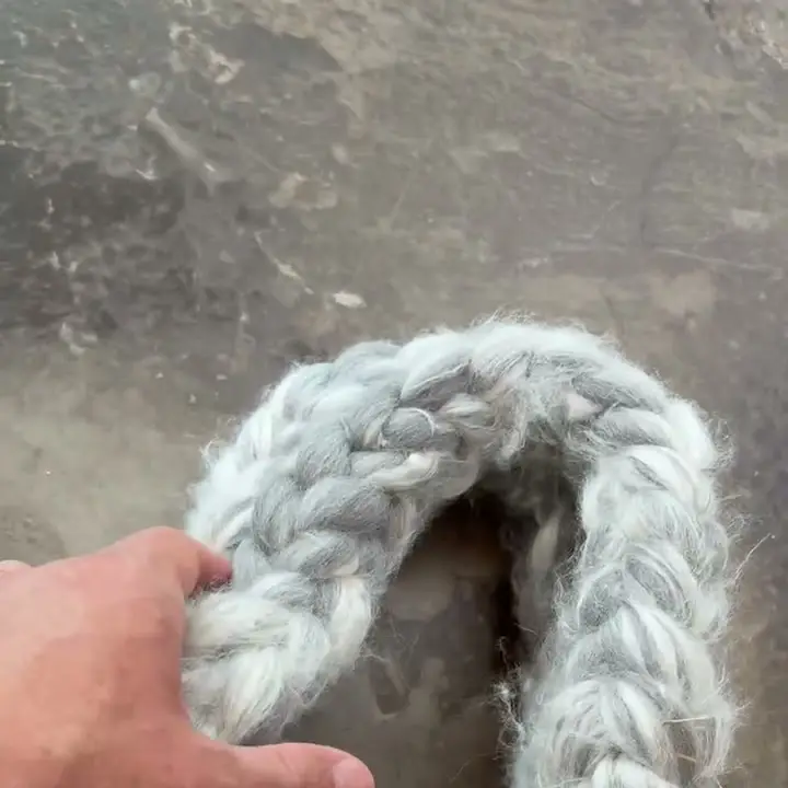 A hand holding the braided i-cord strap of the silver-grey merino-silk bag.