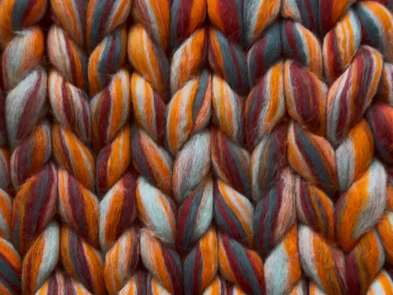 Close-up of a refreshed chunky roving cardigan in rust, burgundy, orange and grey-teal, every stitch edge crisp.