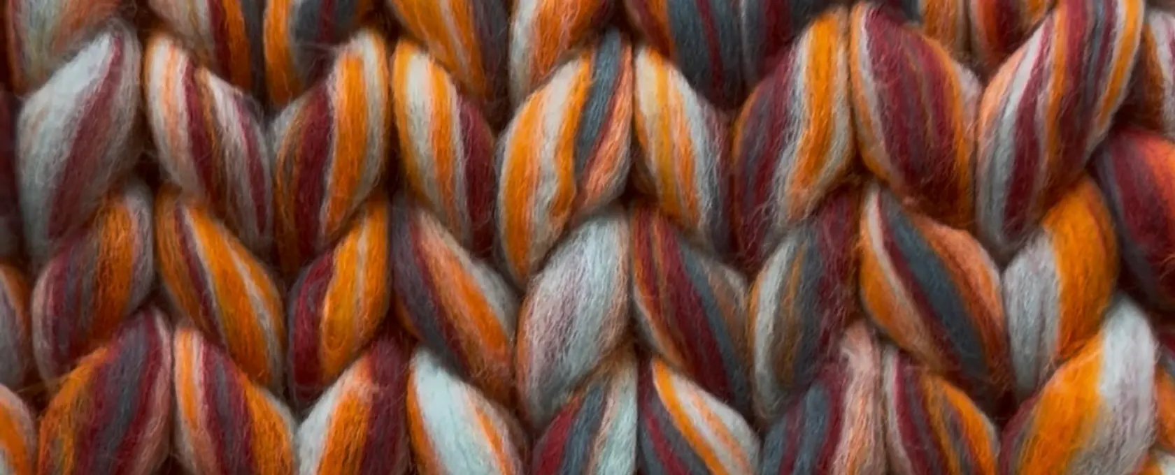 Close-up of a refreshed chunky roving cardigan in rust, burgundy, orange and grey-teal, every stitch edge crisp