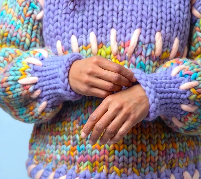 Mani incrociate ai polsi nel Gigante Jumper: i punti filza Eggshell che incorniciano la fascia Lavender e circondano entrambi i polsini.