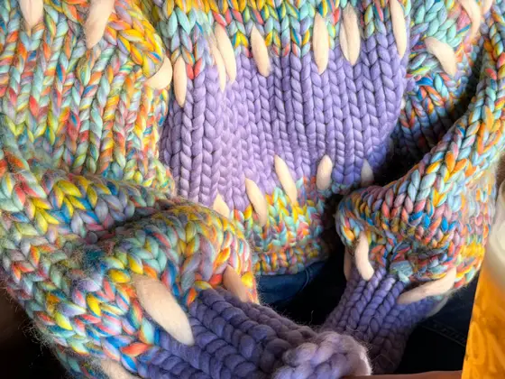 Close-up of the Gigante Jumper: Pastel Rainbow stitches, the Lavender band across the chest and the Eggshell running stitches