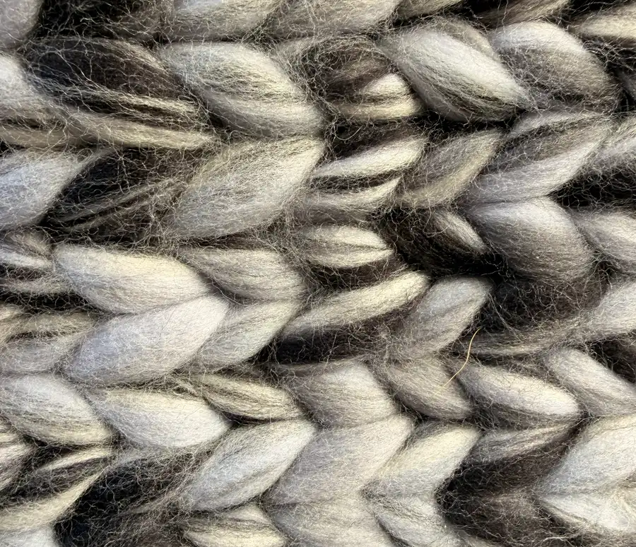 A close-up of chunky knit stitches in alternating charcoal and silver-grey wool, each V-shaped stitch clearly visible.