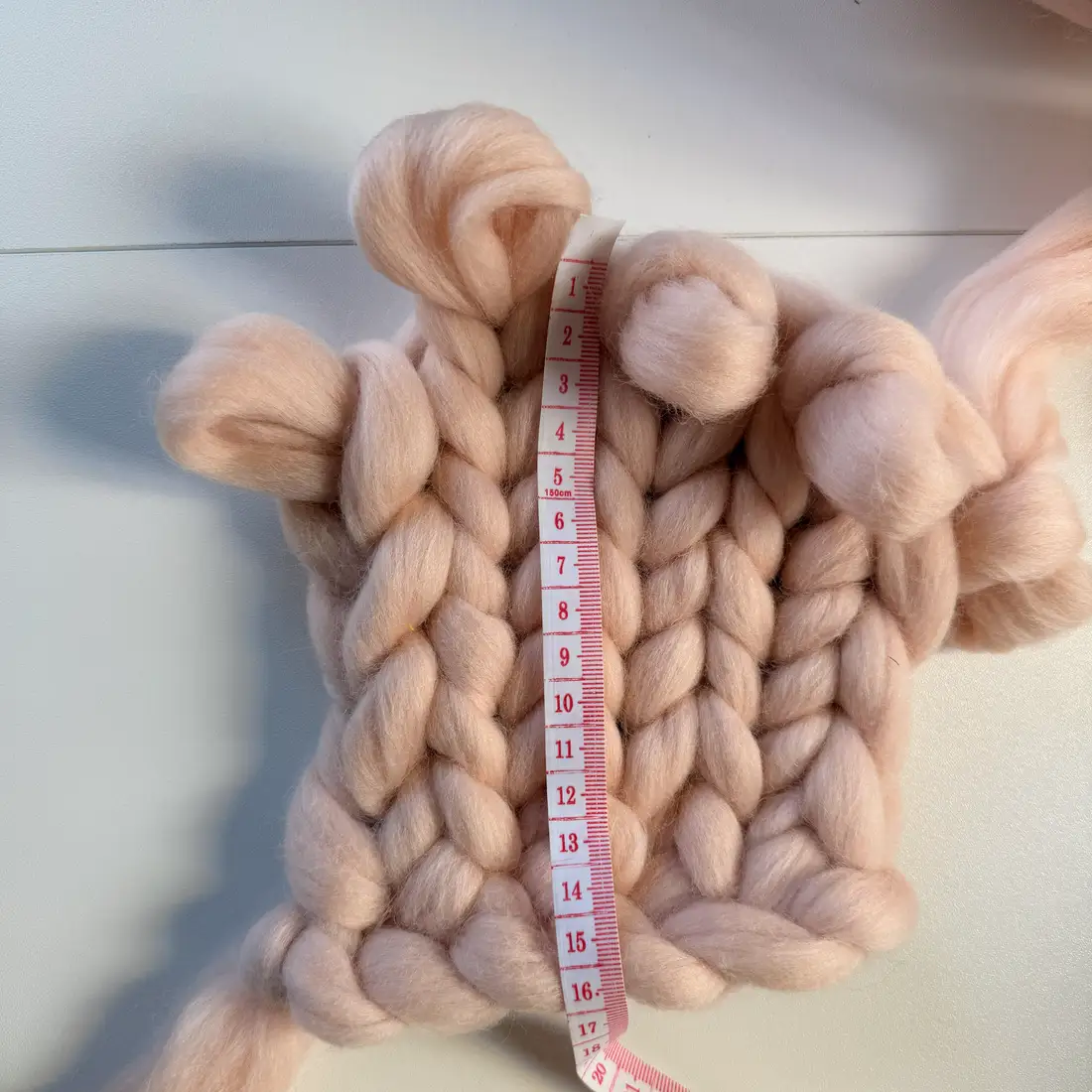 The full 16cm gauge swatch in blush-pink chunky wool laid flat, with a tape measure running down the middle of the stitches.