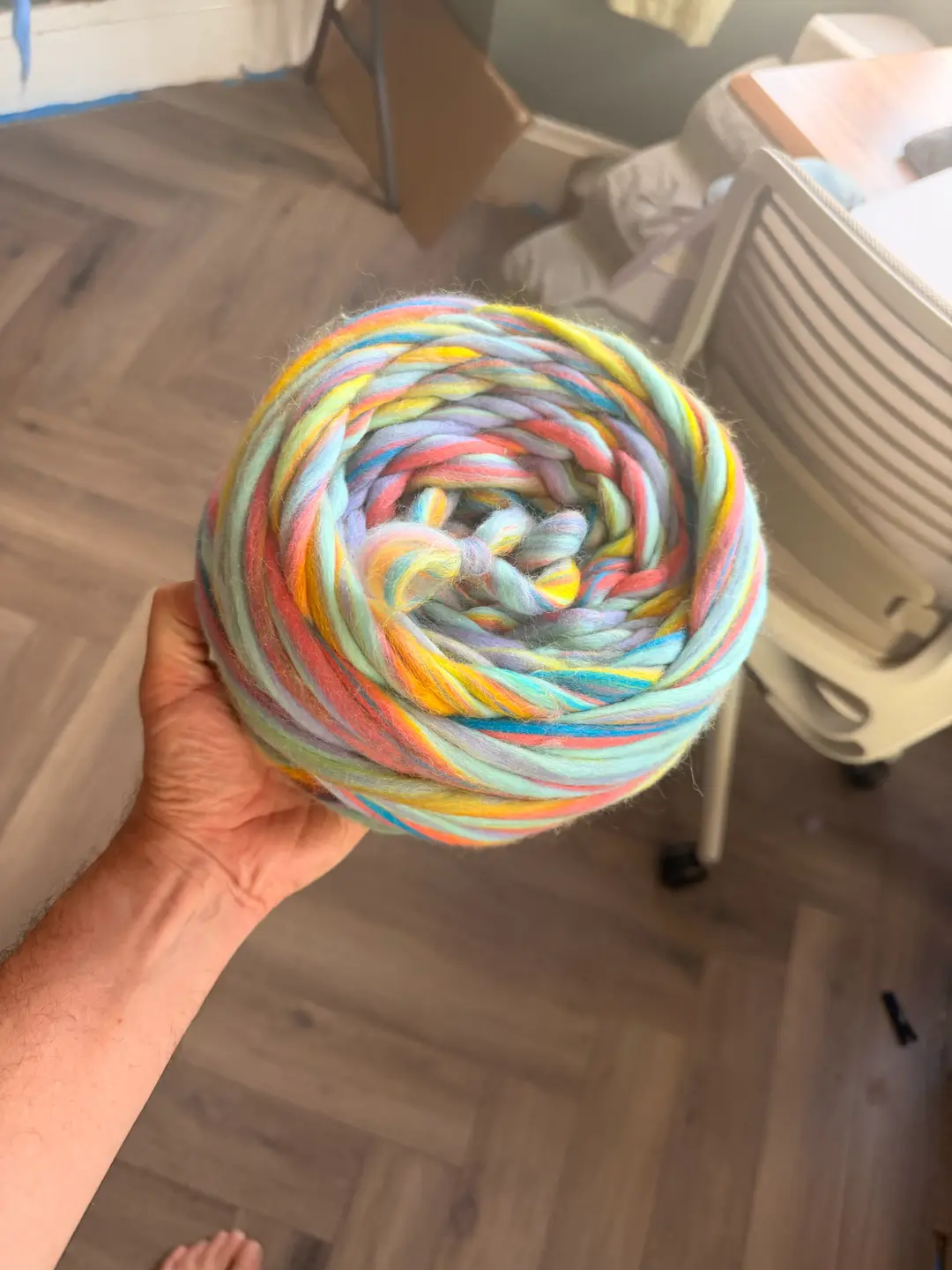 Un gomitolo di Gigante Junior tenuto in una mano, il top di lana non filata Pastel Rainbow diviso e avvolto a ciambella.