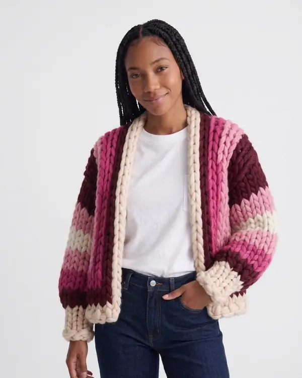 A woman with braids in a chunky knit cardigan in deep wine with bright pink and cream bands, front view.