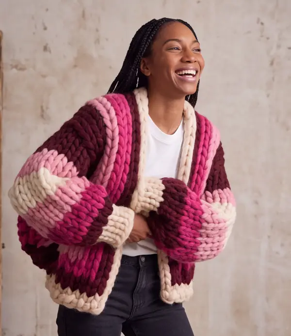 The same woman laughing in the Retro Neon cardigan against a plaster wall.